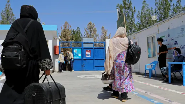 تصویر دو زن بازگشته در یکی از مراکز پذیرش مهاجران وابسته به ملل متحد. این زنان با اندک وسایل دست داشته شان که شامل یک بیک می‌شود راهی افغانستان شده‌اند. یکی از این زنان یک دیک بخار نیز به دستش است. در تصویر چند مأمور کارمند در این مرکز نیز به چشم می‌خورند. 