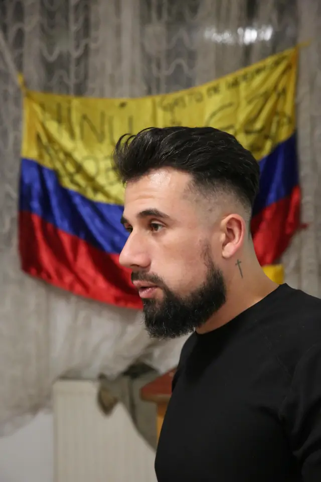Árabe está parado de perfil, con una bandera colombiana detrás de él.