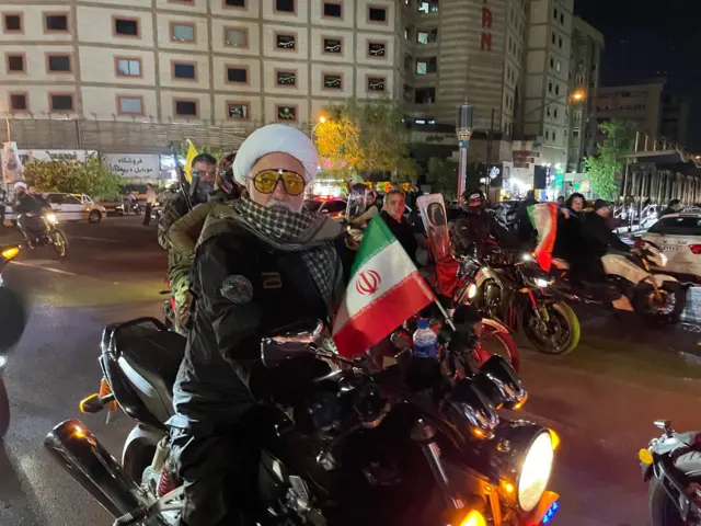 Sekelompok pria bersenjata mengendarai sepeda motor sambil mengibarkan bendera Iran di pusat kota Teheran.