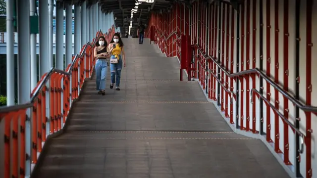 ผู้หญิง 2 คนกำลังเดินบนทางเชื่อมสกายวอล์กสู่สถานีรถไฟฟ้าบีทีเอส