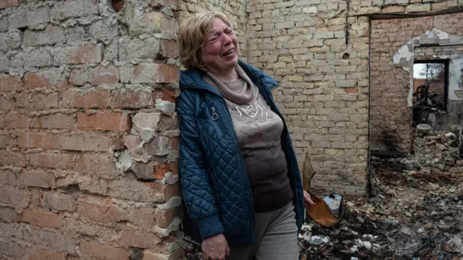 A woman cries inside her burnt house in Ozera, Ukraine