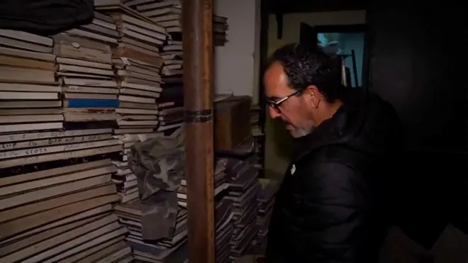 Feras Kilani looks at piles of books in a darkened room