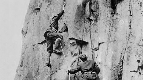 Black-and-white photo of men ascending a mountain rock in the Alps