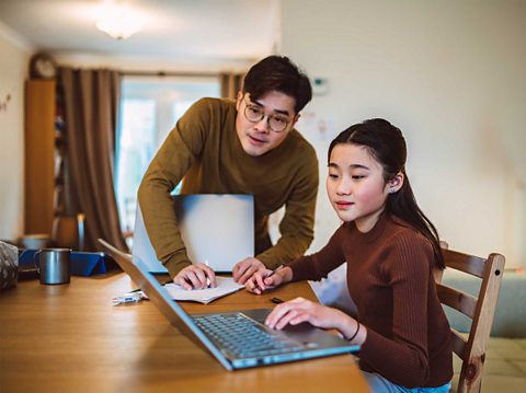 A photo of a father teaching his daughter at the table working on a laptop. 