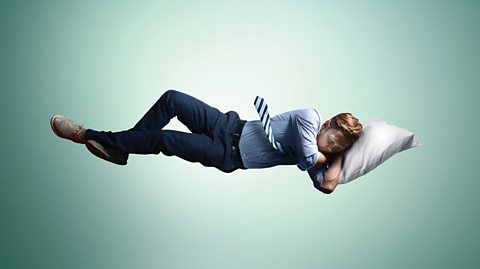 A man in a suit sleeps whilst floating in mid-air.