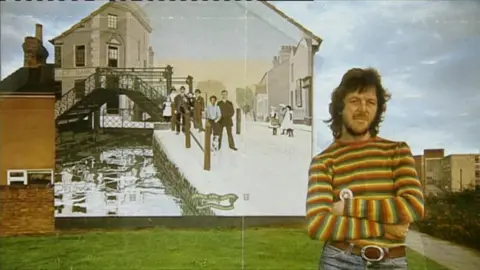 Ken White seen in the 1970s standing in front of a new created mural.