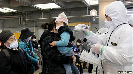 An official in a radiation protection suit scans a mother and child with a geiger counter to check radiation levels